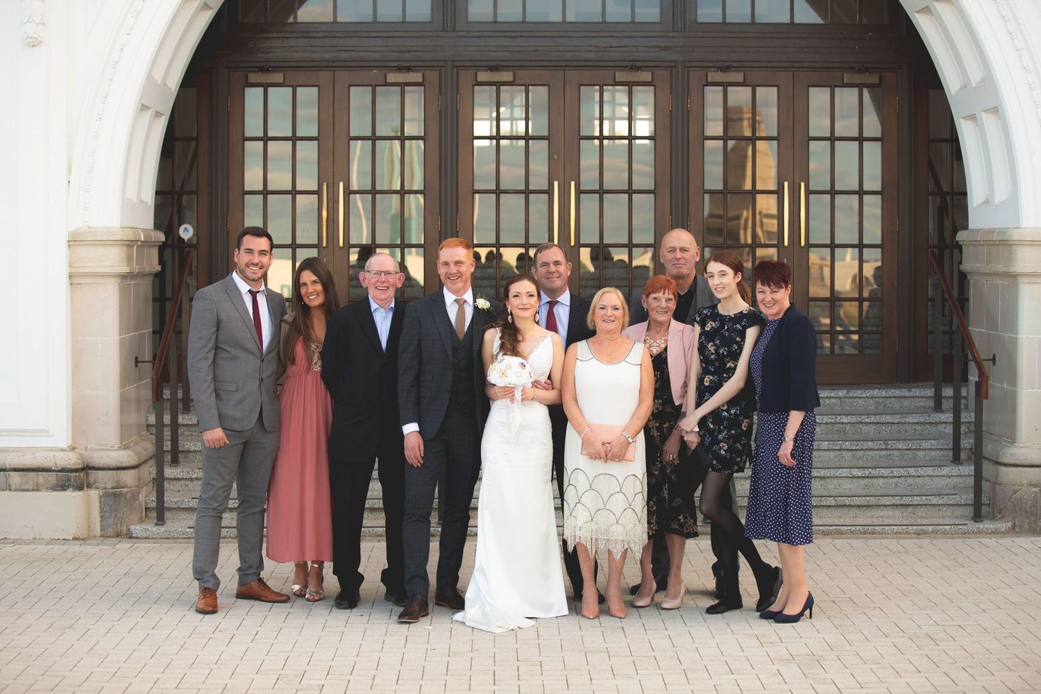 Wedding party gathered for formal portrait outside historic building entrance with arched doorway.