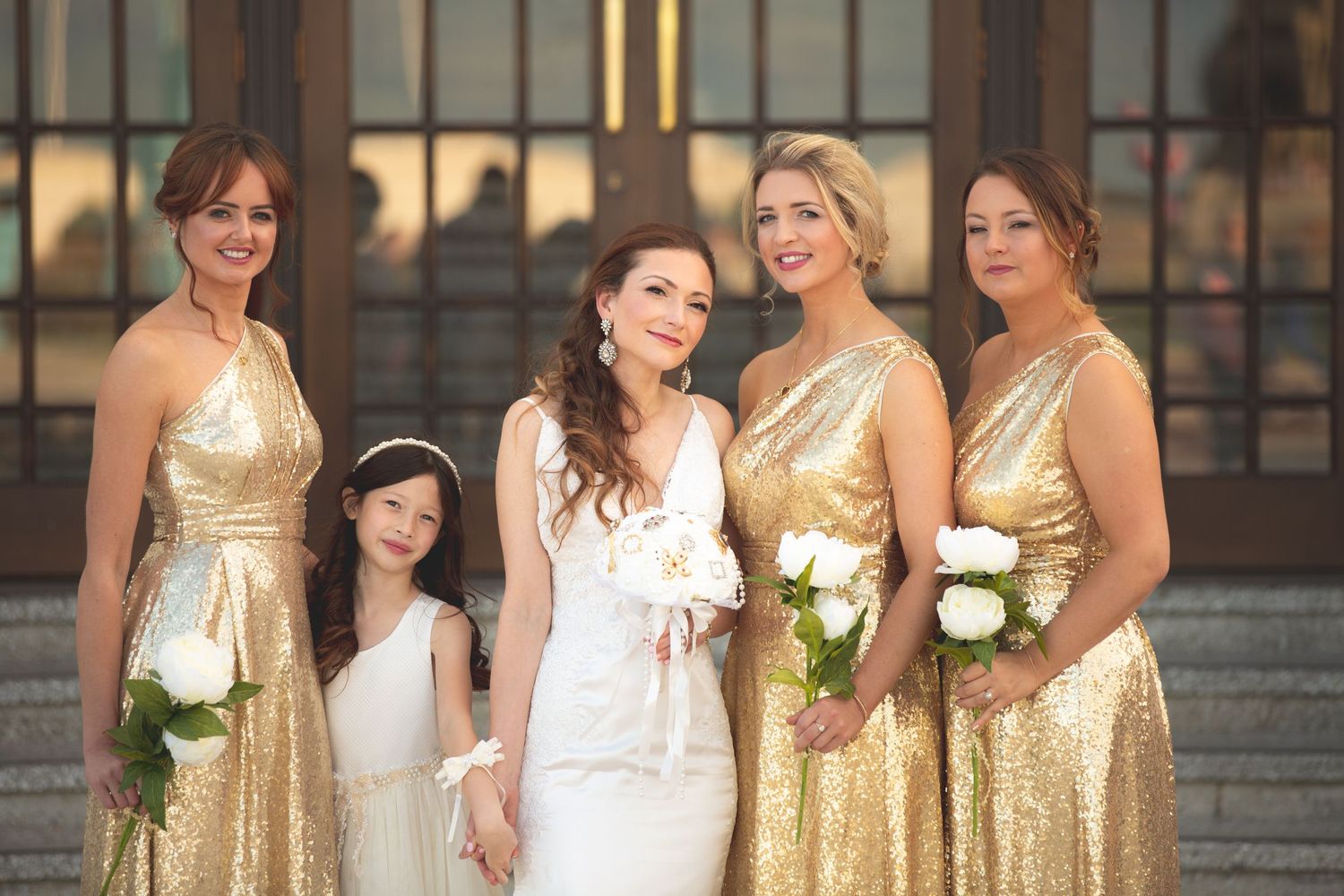 Bridal party in shimmering gold dresses poses together on stone steps at dusk.