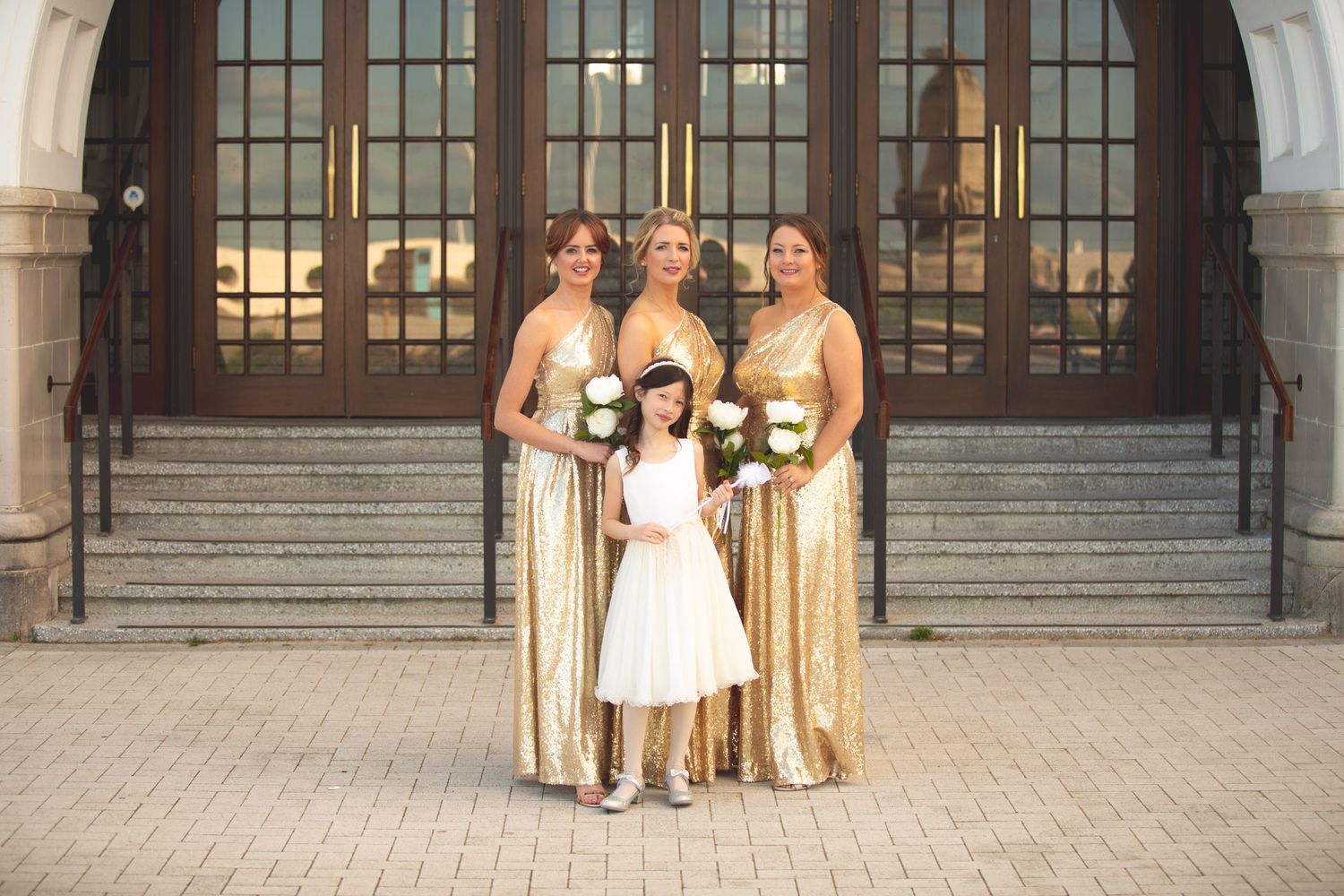 Wedding party poses on stone steps with bridesmaids in gold dresses and flower girl in white.