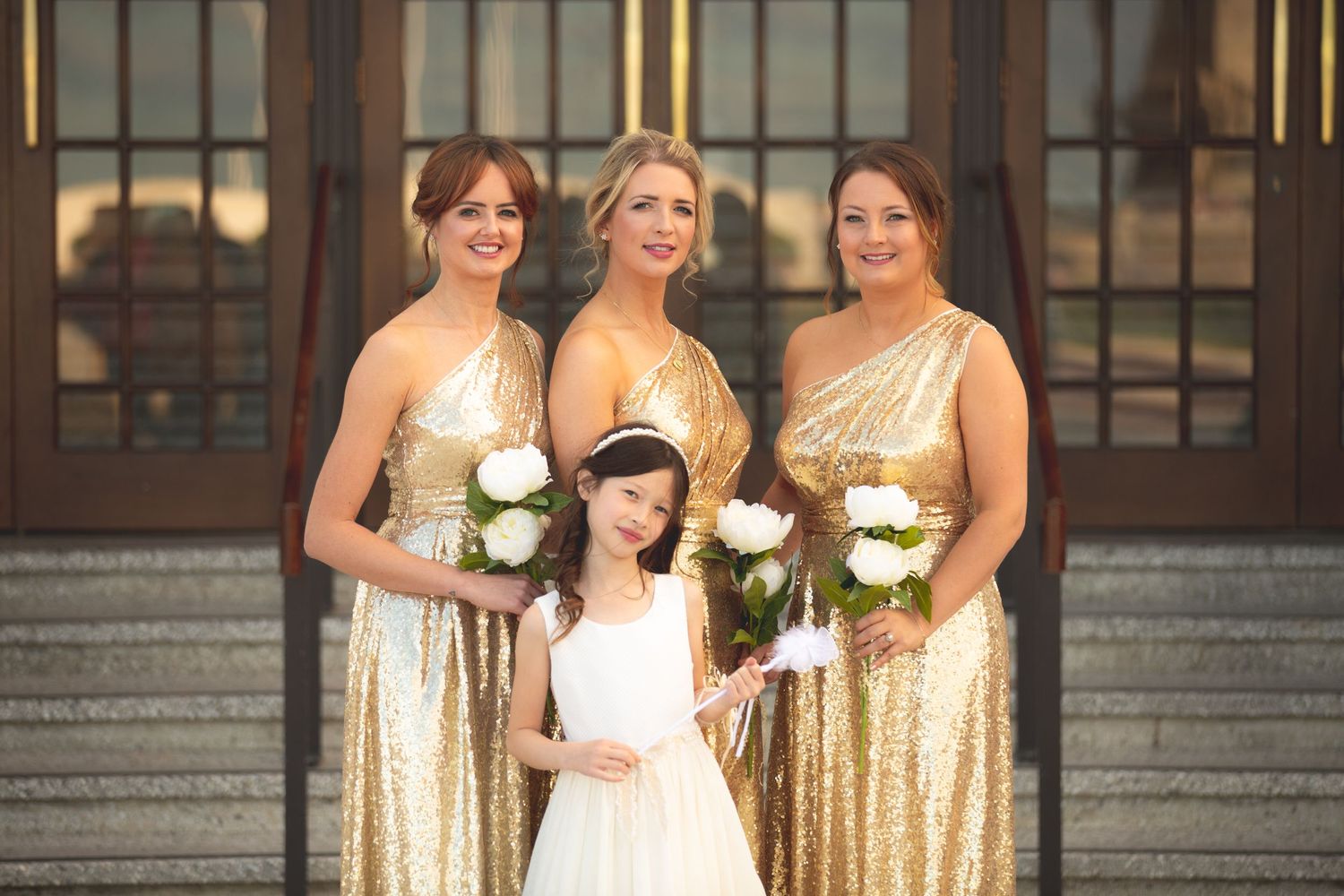 Bridal party wearing gold sequin dresses poses with young flower girl in white.