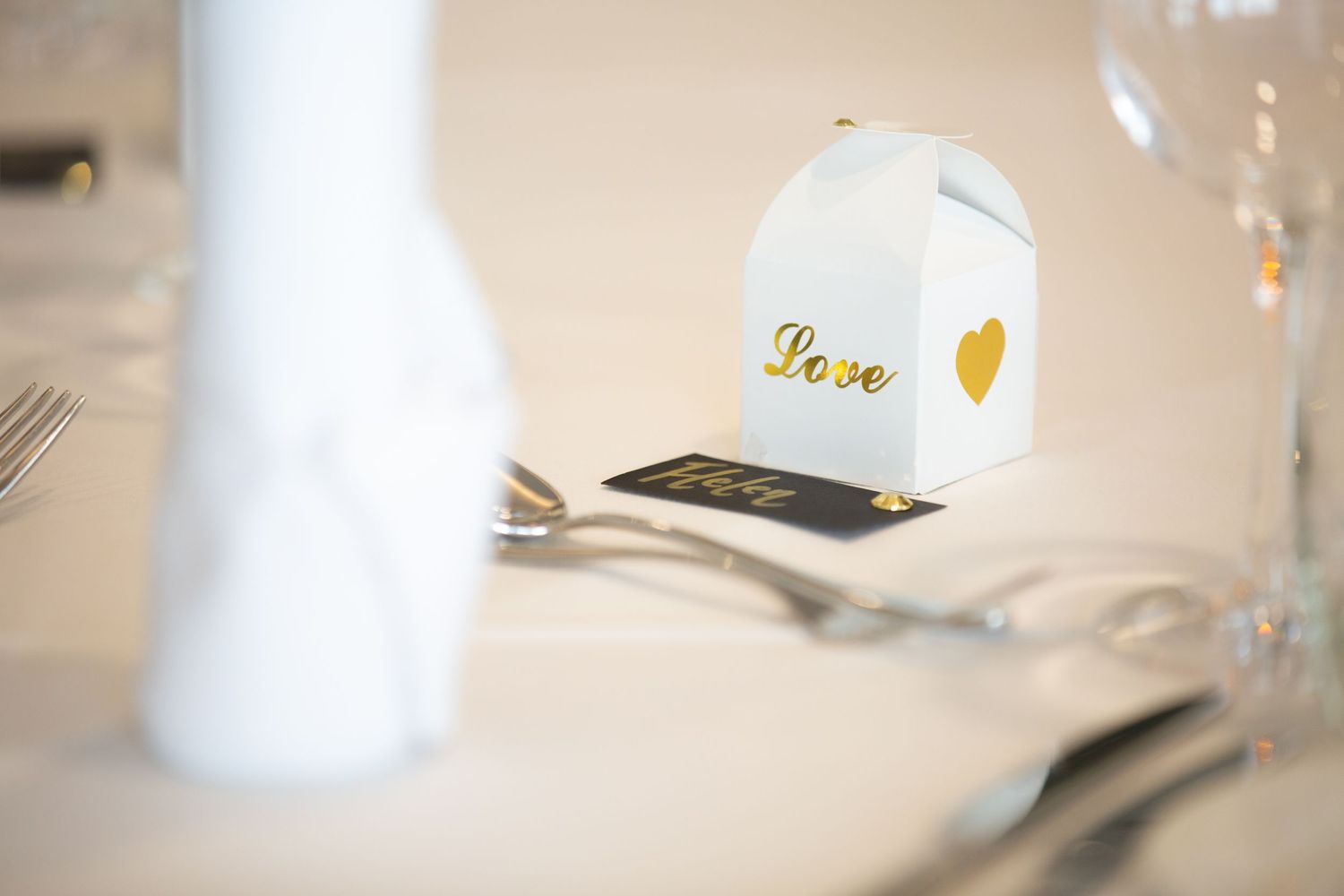 White place card holder with gold heart detail sits on elegant table setting.