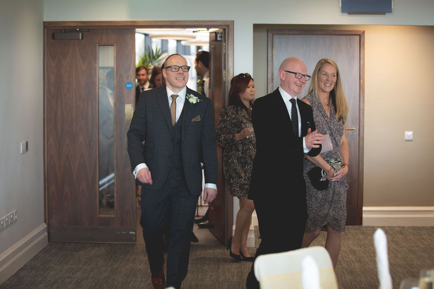 Wedding guests entering reception hall through wooden double doors.