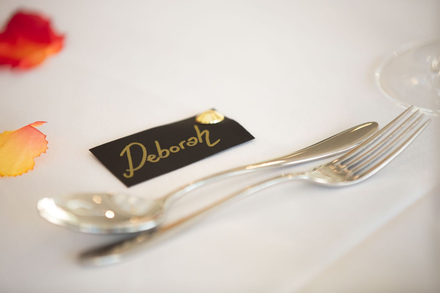 Close-up of silver cutlery and place card on white tablecloth at wedding reception.