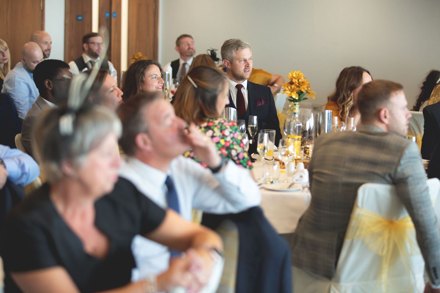 Wedding reception guests laugh and enjoy themselves at decorated tables with sunflower centerpieces.