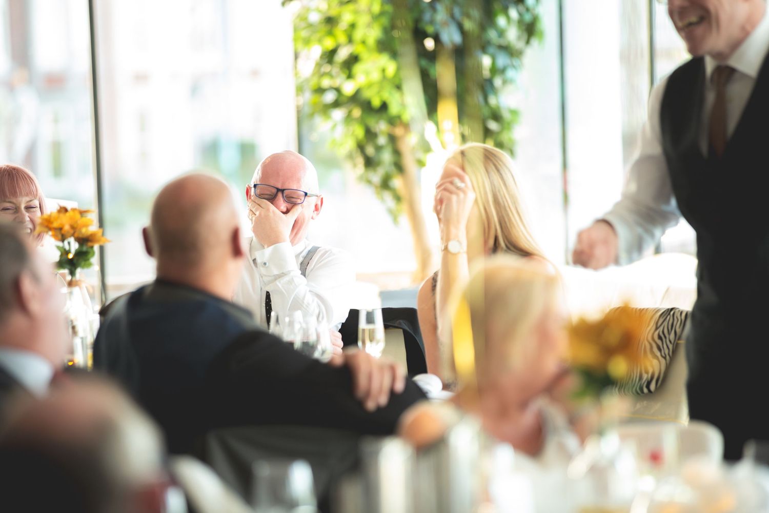 Guests celebrate and socialize at a bright, window-lit wedding reception.