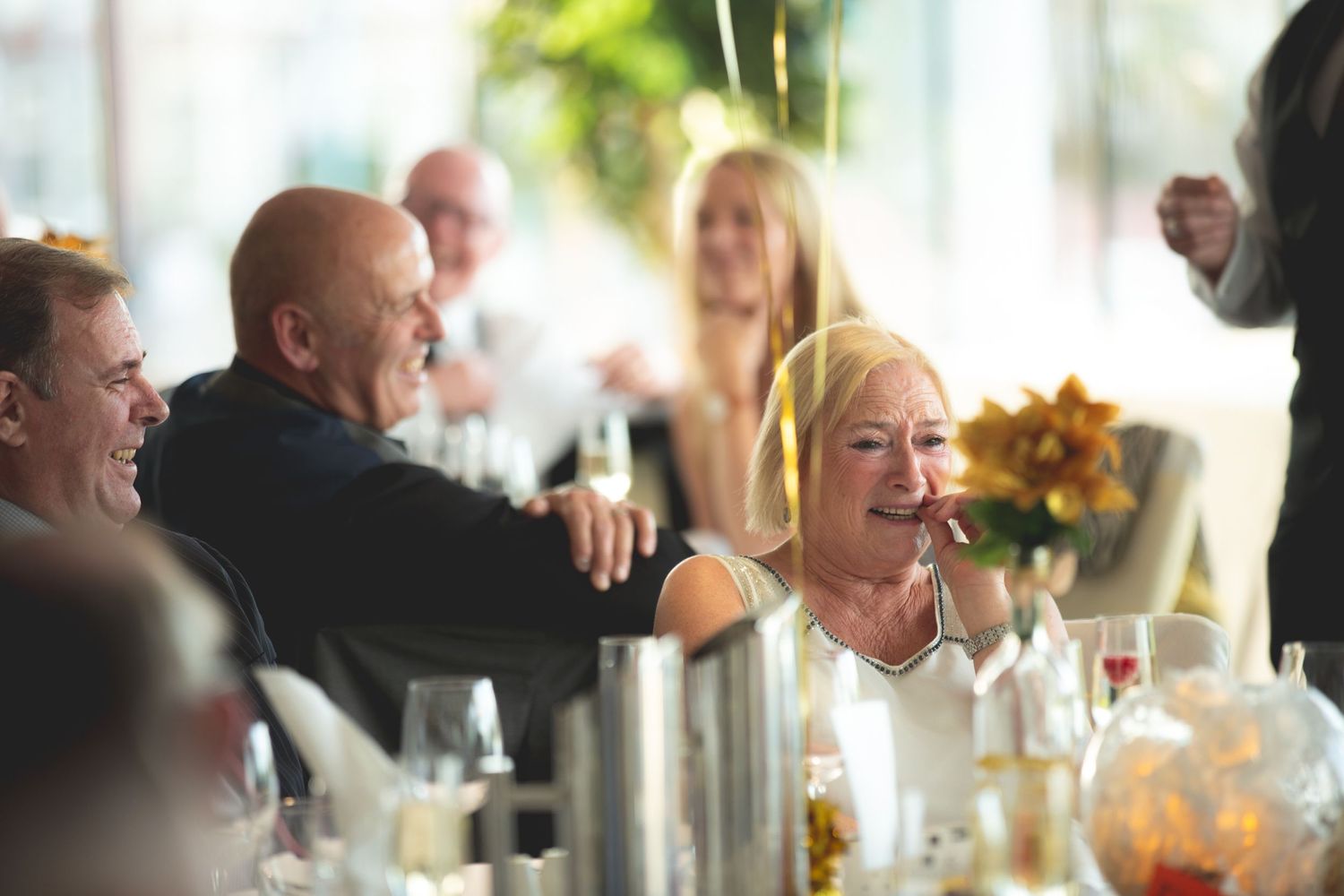 Guests laugh and enjoy themselves at a formal dining event with wine glasses and table settings.