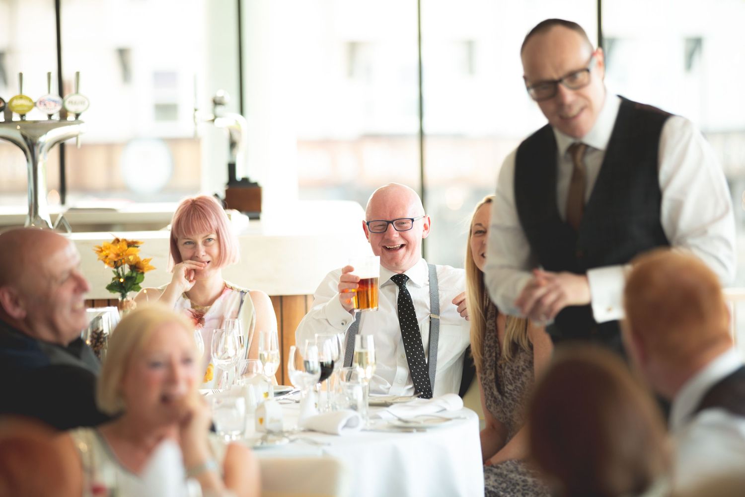 A server in formal attire interacts with dinner guests at an elegant white-tablecloth restaurant.
