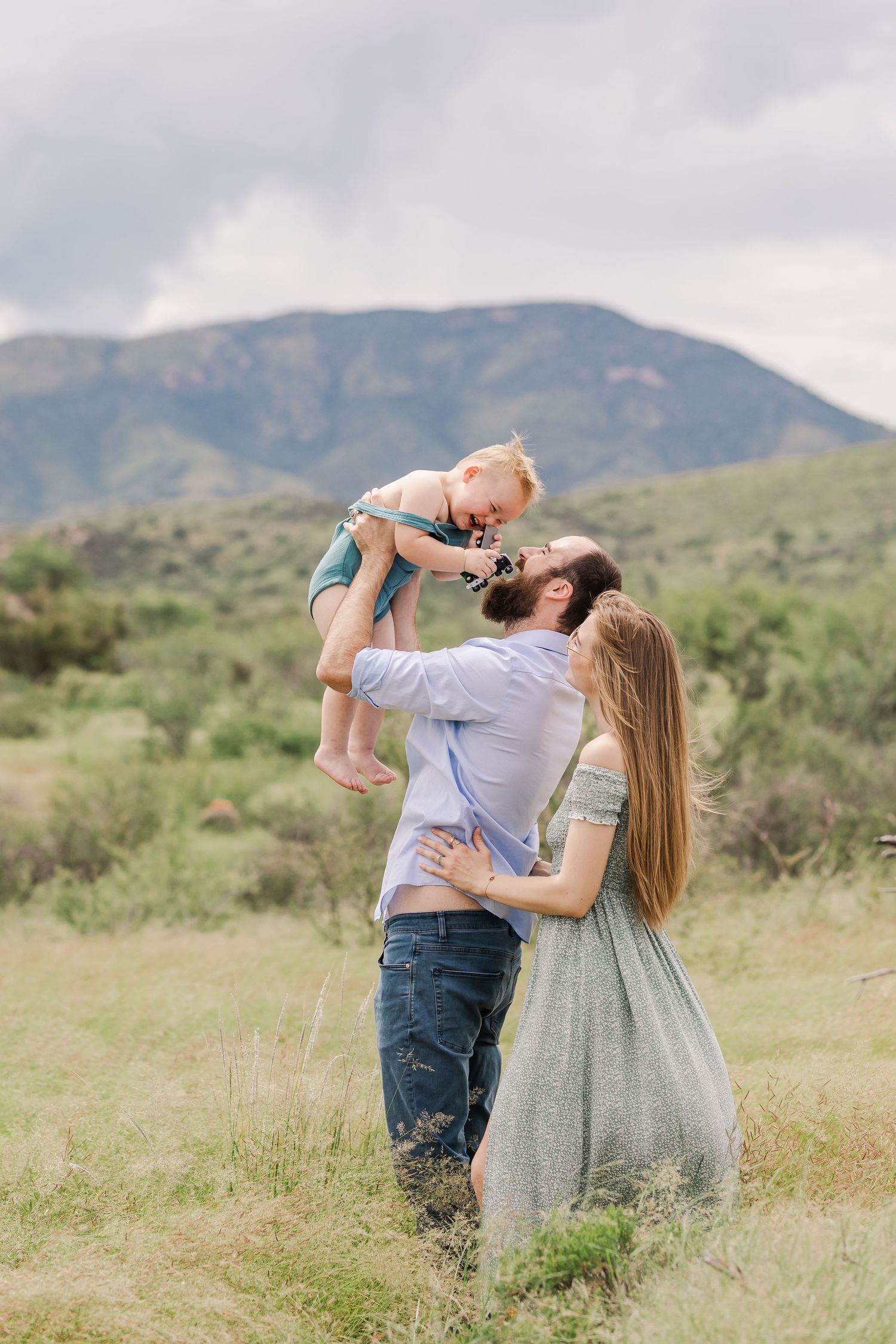 Portrait of a father holding his toddler son in the air while mom looks on, smiling
