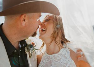 Candid wedding moment captured with bride and groom laughing together under bright sunlight.