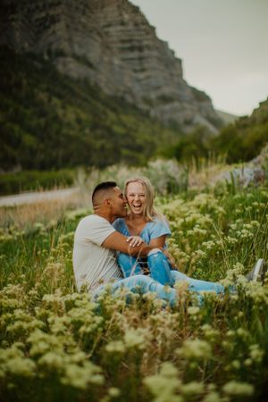Couple sharing joyful moment in wildflower meadow with mountain backdrop.