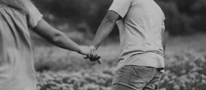 Black and white image of two people holding hands while walking.