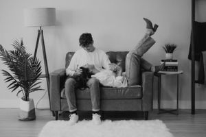 A black and white candid moment of relaxation on a grey couch with houseplants in the background.