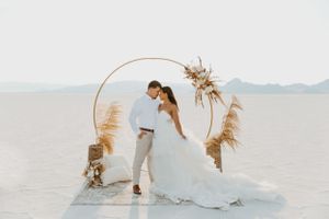 Desert wedding scene with couple posing under circular arch decorated with pampas grass.