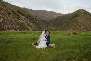 A couple in wedding attire poses in a green valley surrounded by rolling hills.