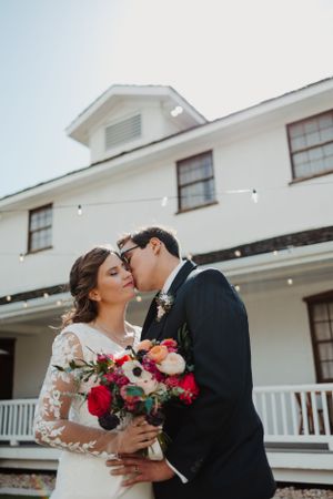 A romantic wedding couple sharing a tender kiss in front of a white building.