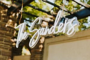 Illuminated neon sign reading 'The Garden' mounted on brick wall with greenery overhead.