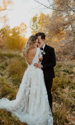 A couple embraces in an autumn field with a detailed lace wedding dress catching golden light.
