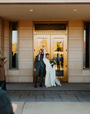 Elegant couple poses outside modern building entrance with glass doors and stone facade.