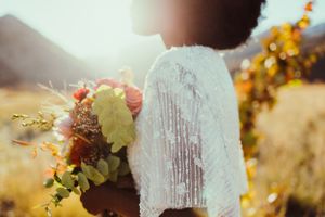 Close-up detail of lace wedding dress sleeve and romantic floral bouquet in golden sunlight.