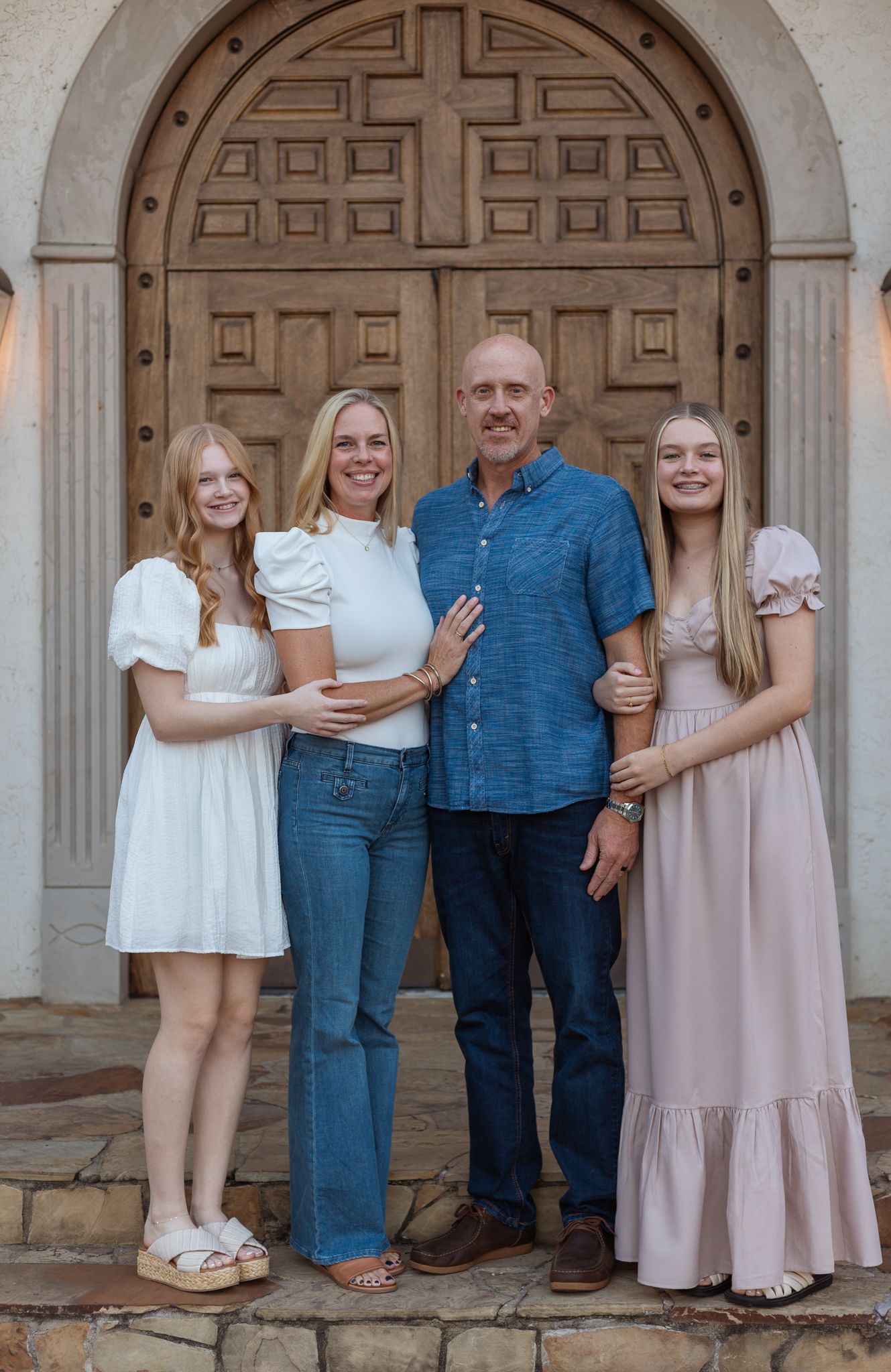 Family portrait in front of ornate wooden church doors with architectural details.