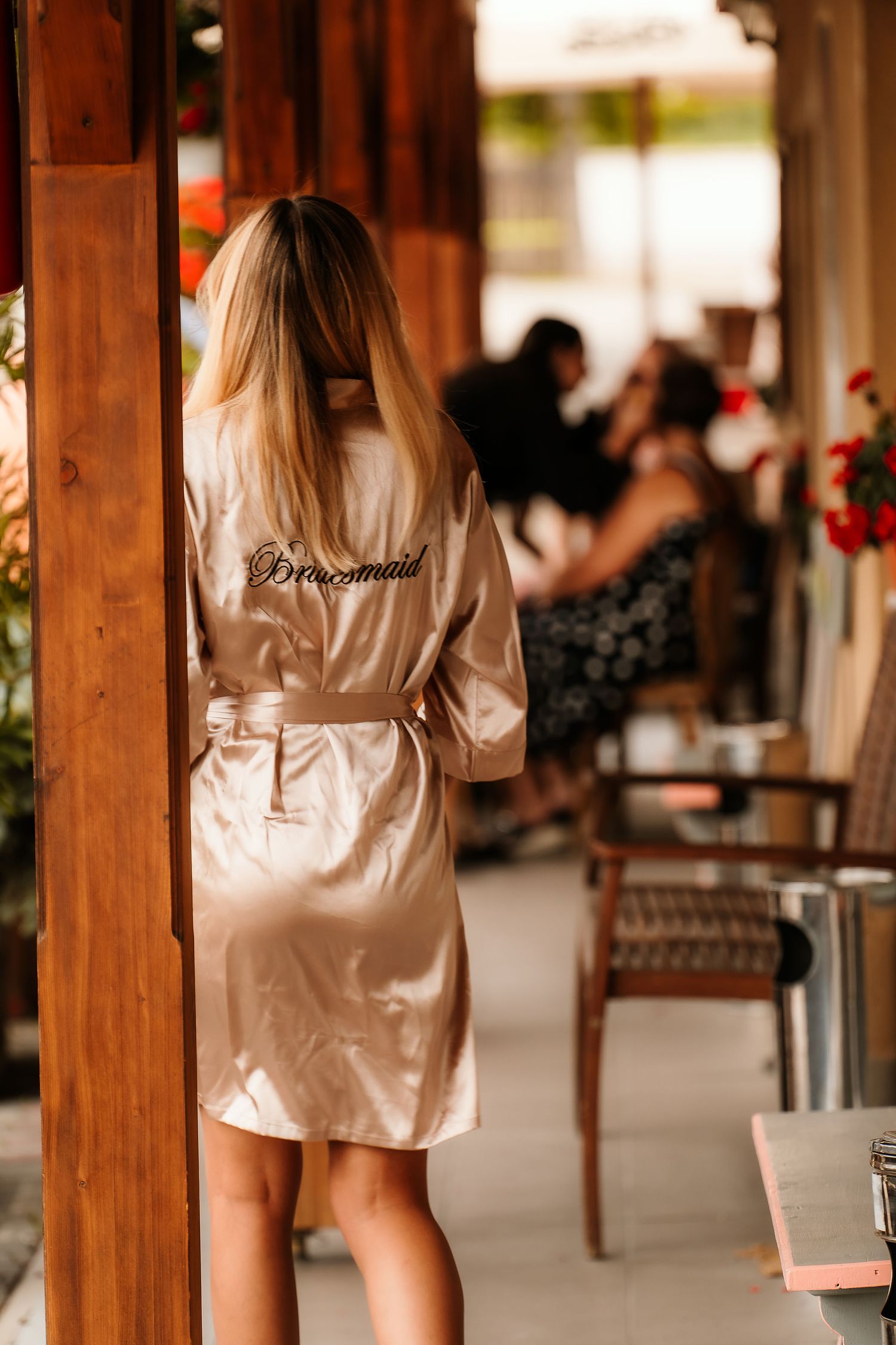 Person in silk robe standing on a covered patio with wooden beams and floral decor.