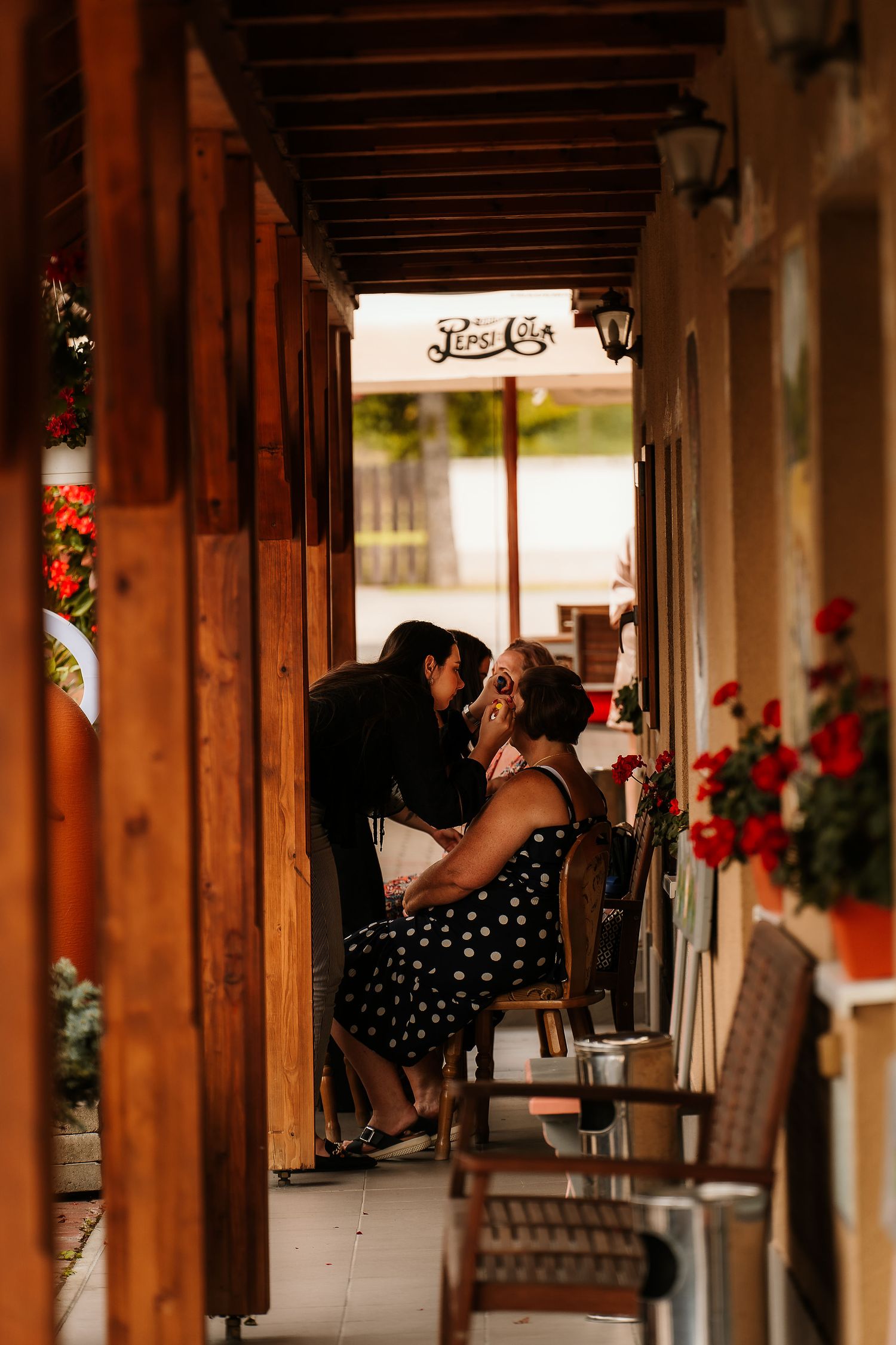 People enjoying conversation in a cozy covered porch with red flowers and wooden beams.