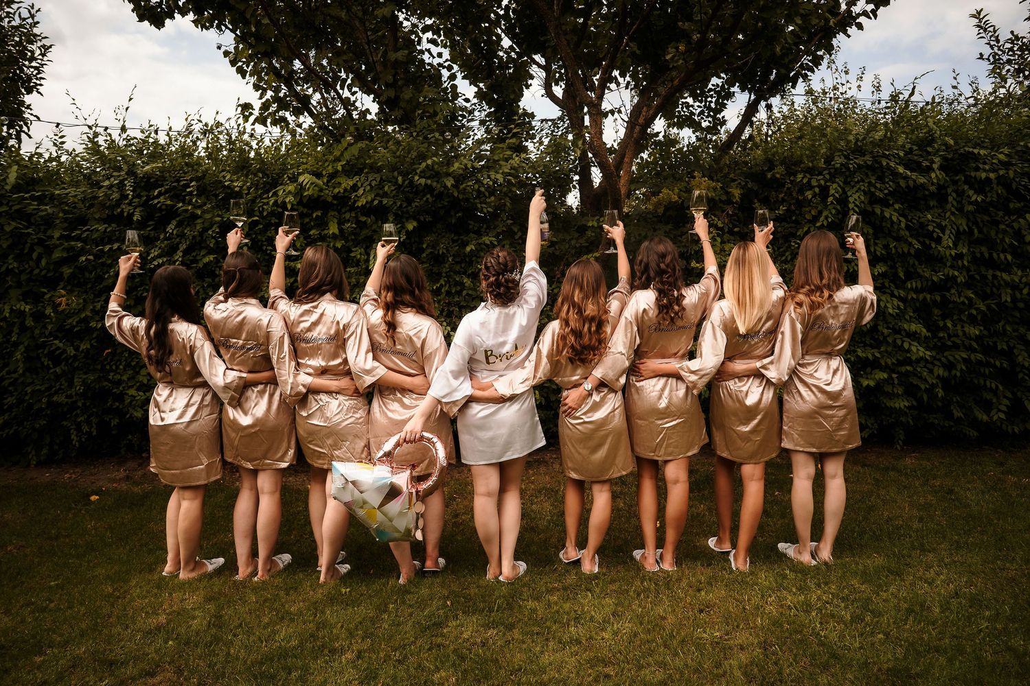 Back view of group in matching silk robes posing together on lawn with small dog.