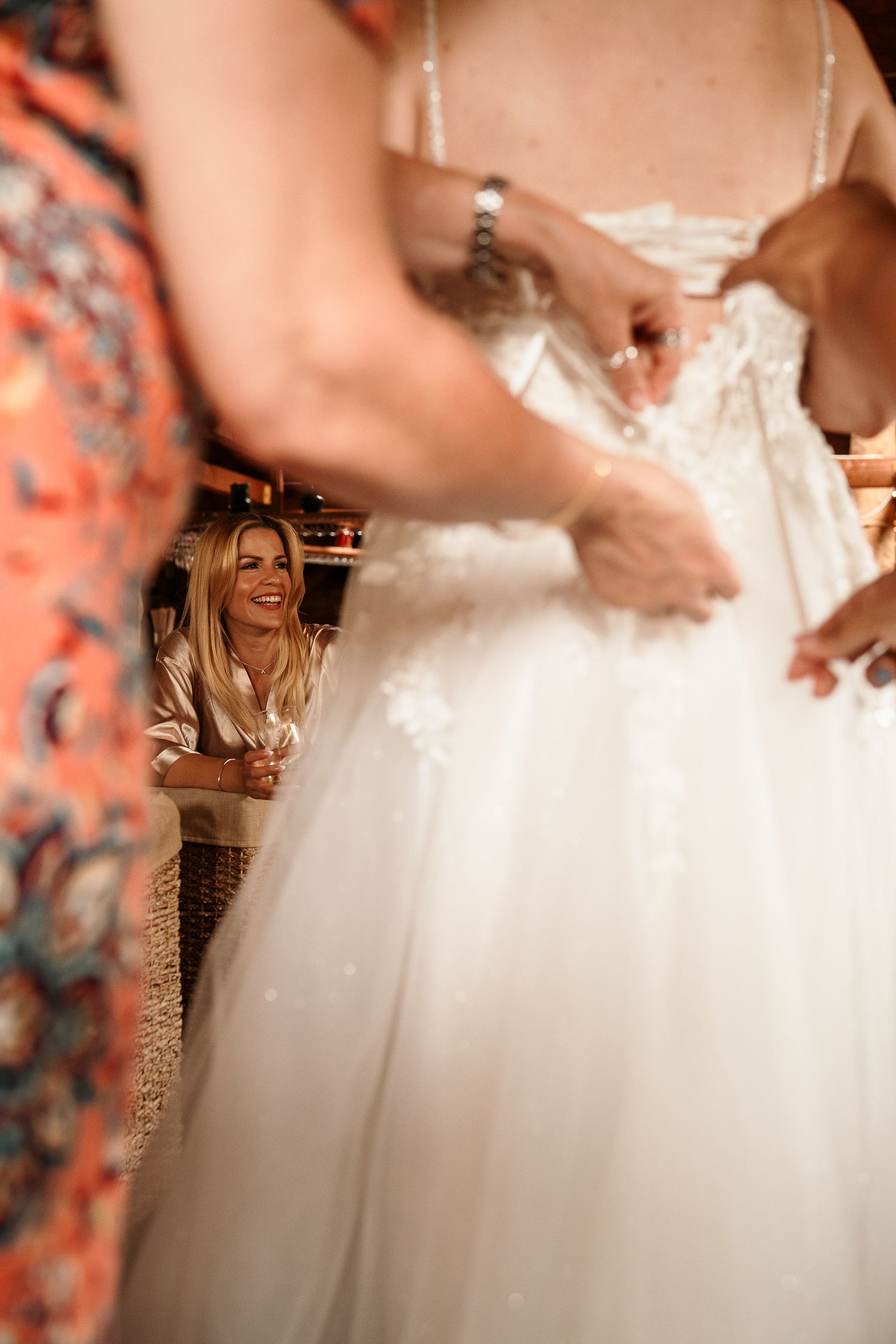 Close-up shot of wedding dress being adjusted with blurred figures in background.