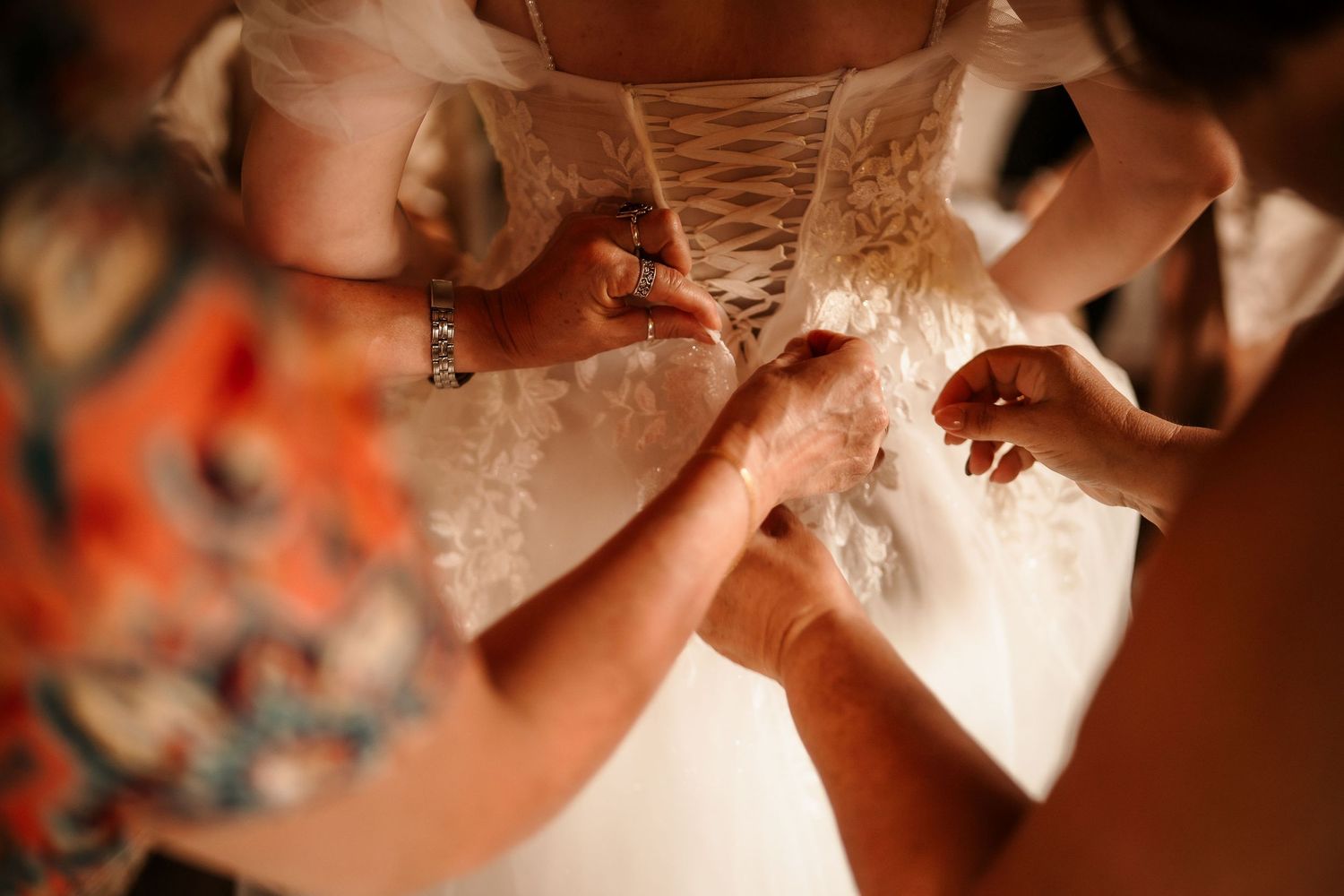Close-up detail shot of hands lacing up back of wedding dress.