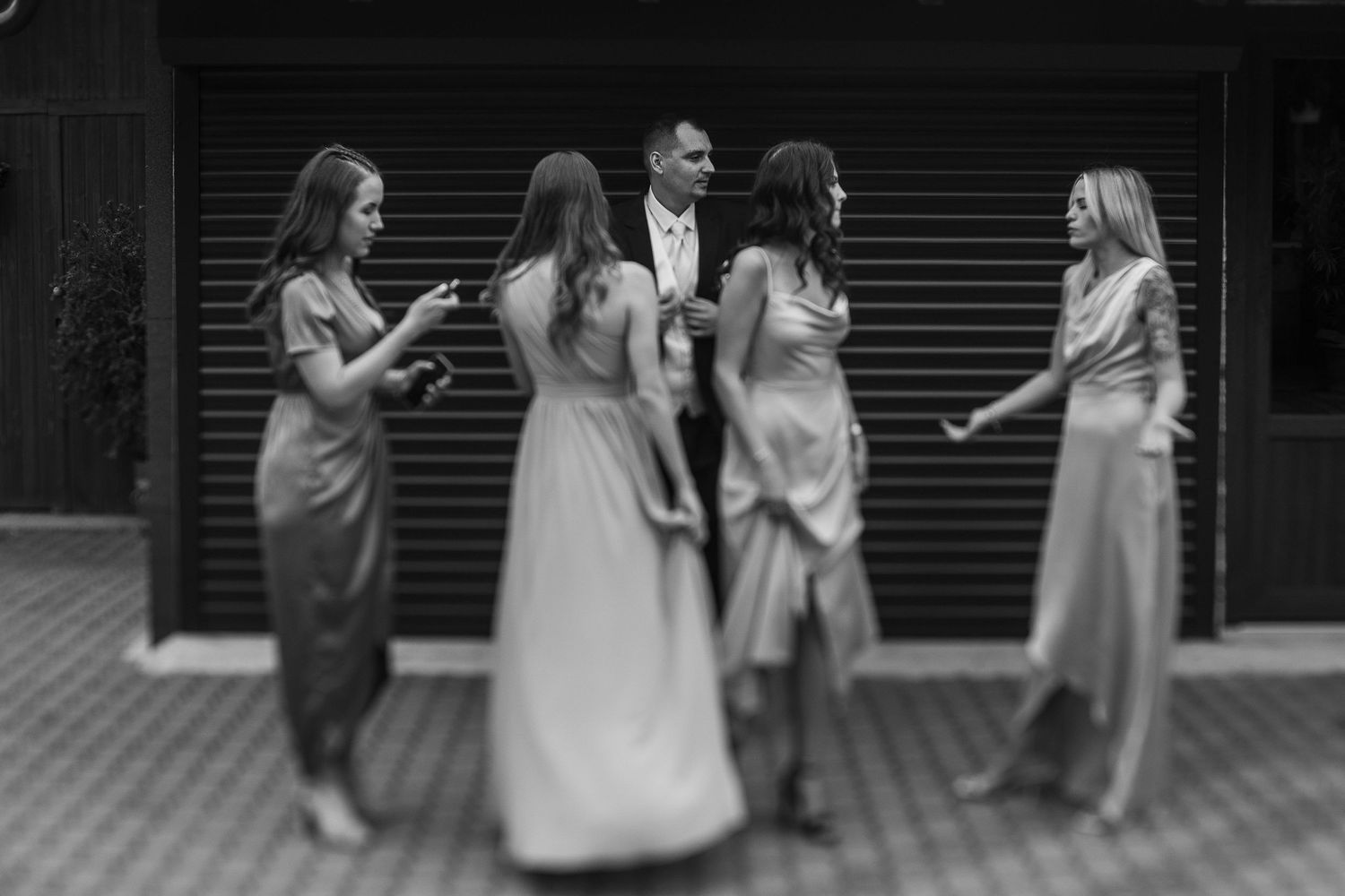 A wedding party in elegant dresses gathers for a casual black and white moment.