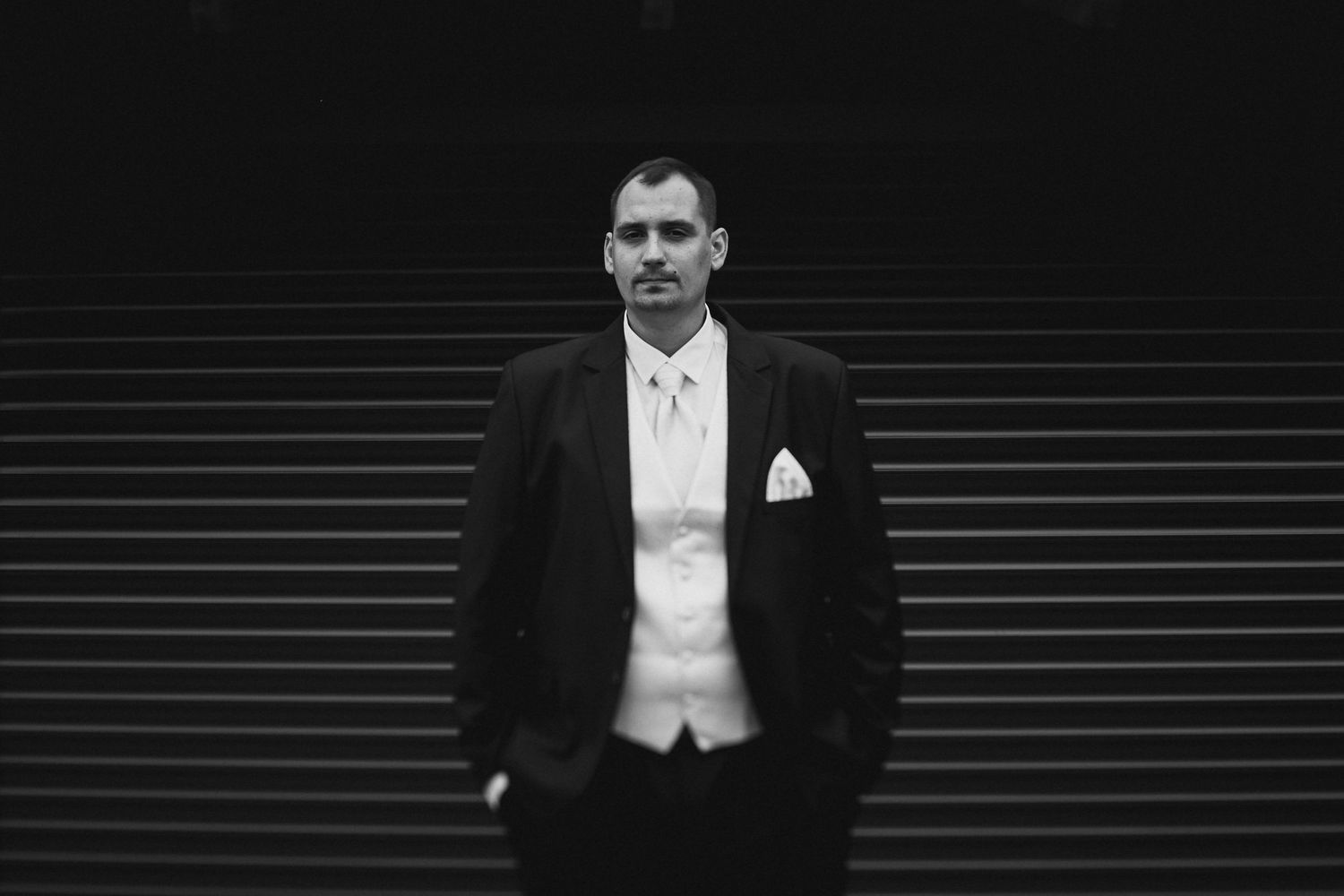 Black and white formal portrait against dark background with dramatic lighting.