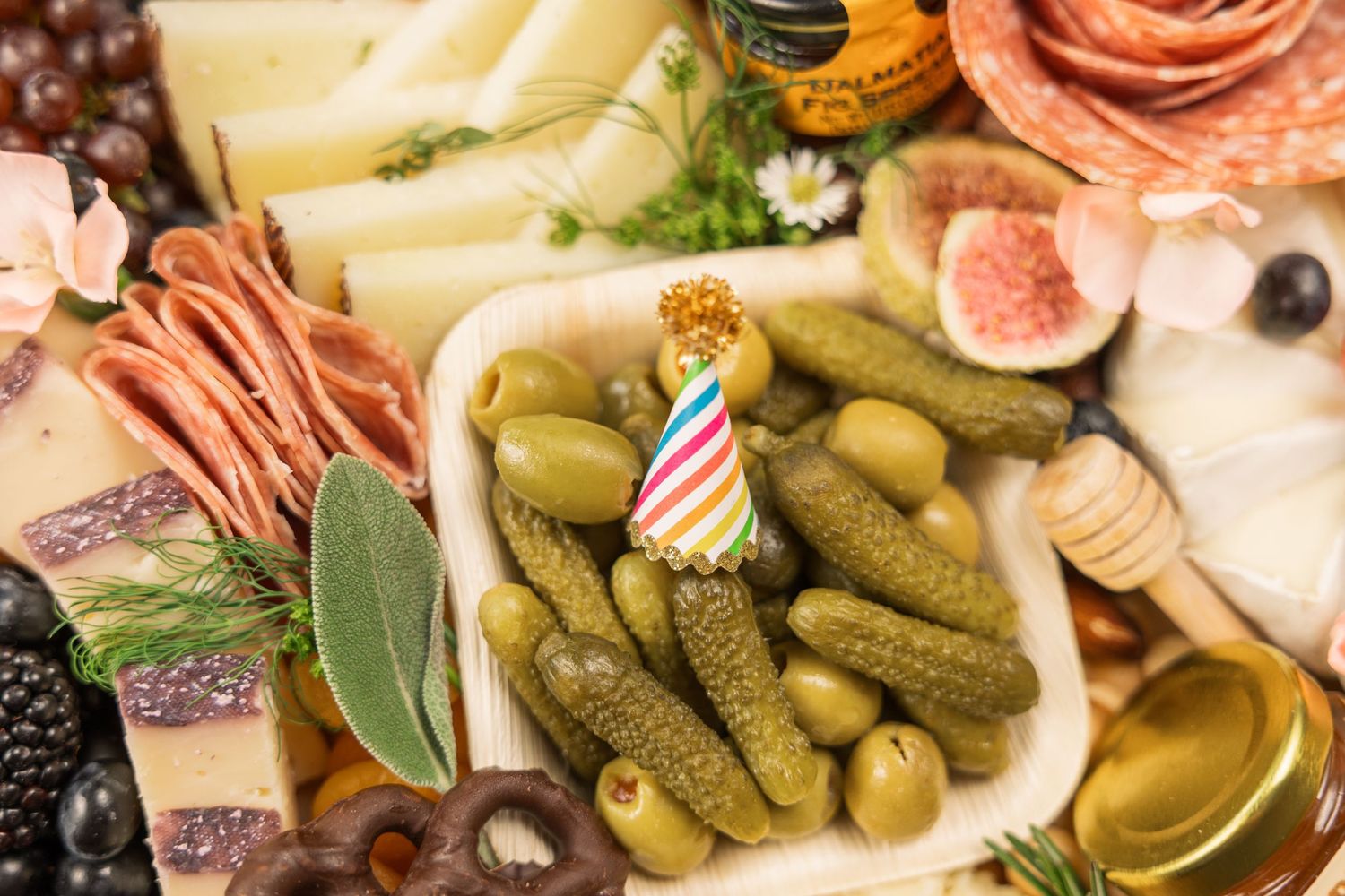 Charcuterie board featuring pickles, olives, and meats with a festive birthday candle decoration.