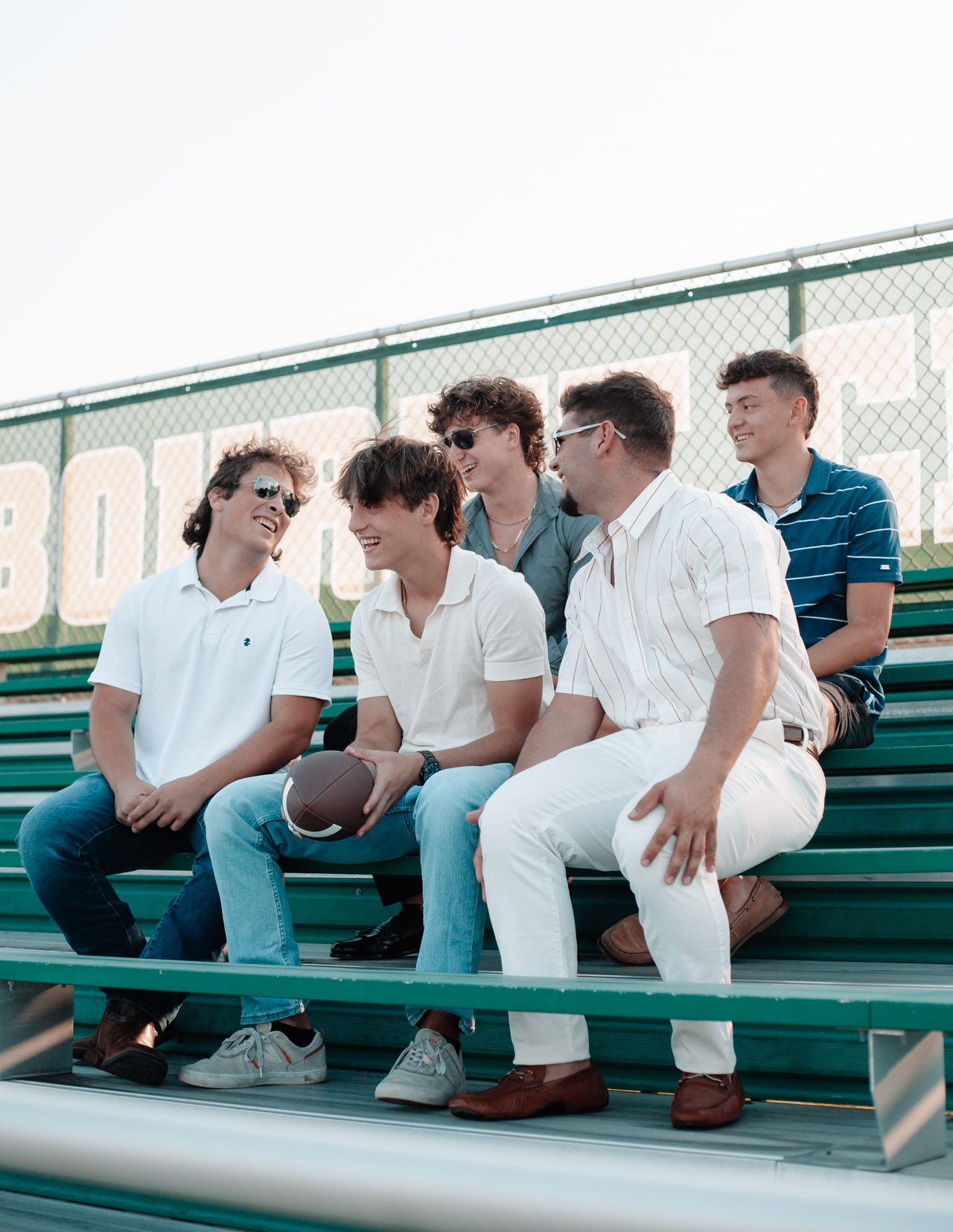 Group of young men sitting on green bleachers in casual white attire.