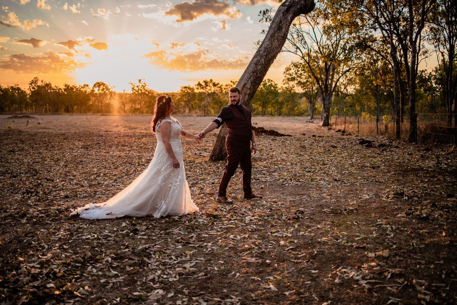 A newlywed couple holding hands during sunset in a rustic outdoor setting.