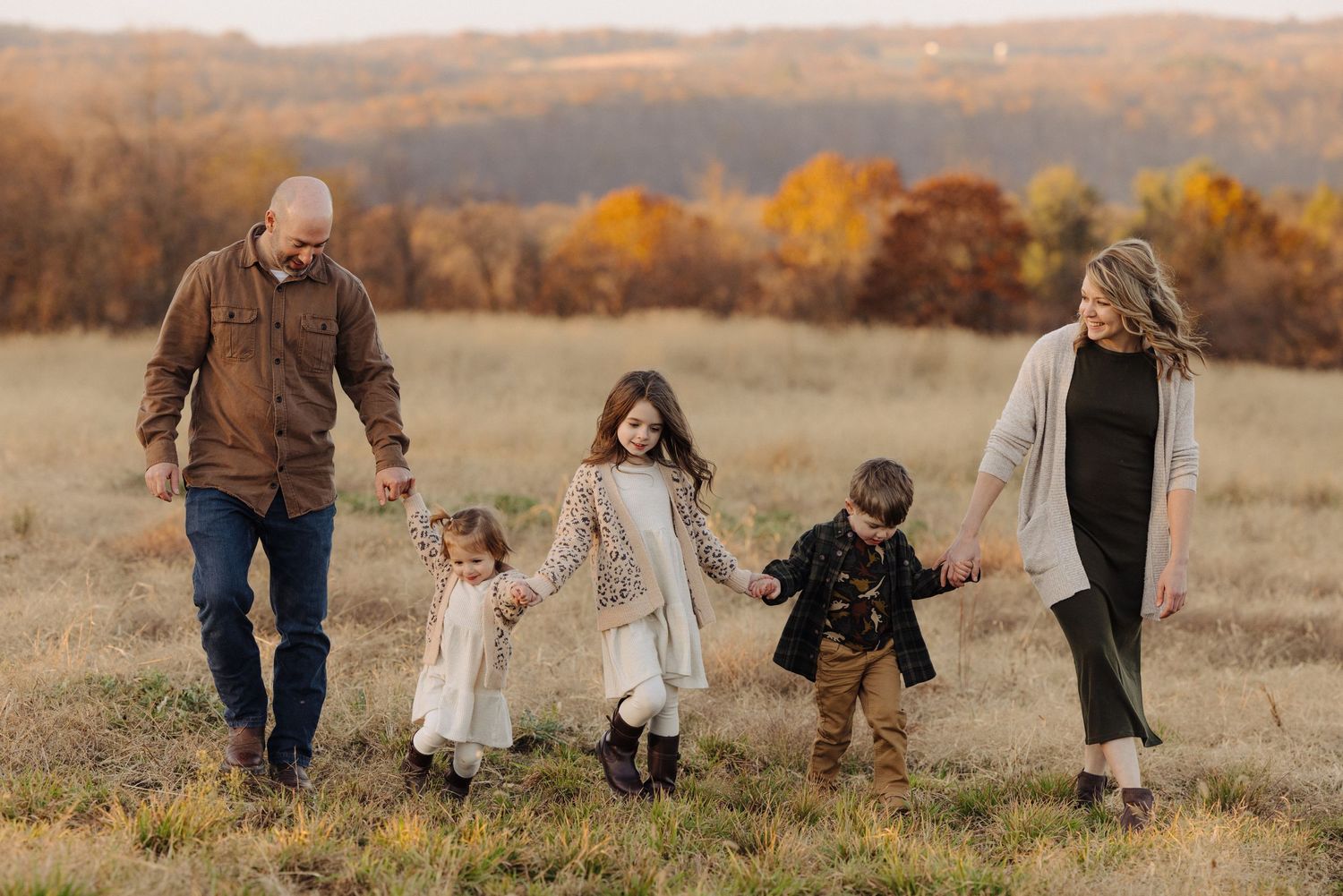 Family holding hands while walking through autumn field at sunset.