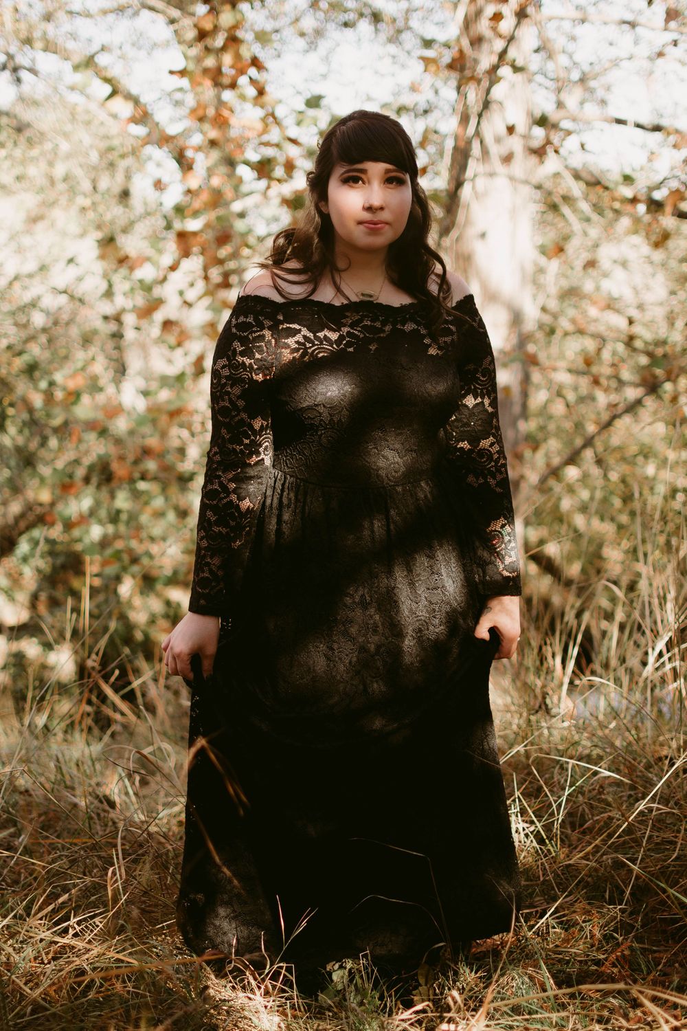 A gothic-style photo of someone wearing a black lace dress in an autumn forest setting.