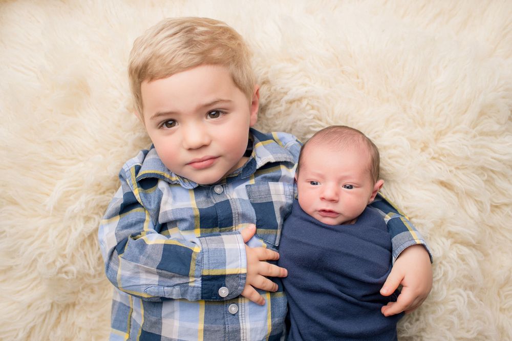Two small children resting together on a soft cream colored fur blanket.