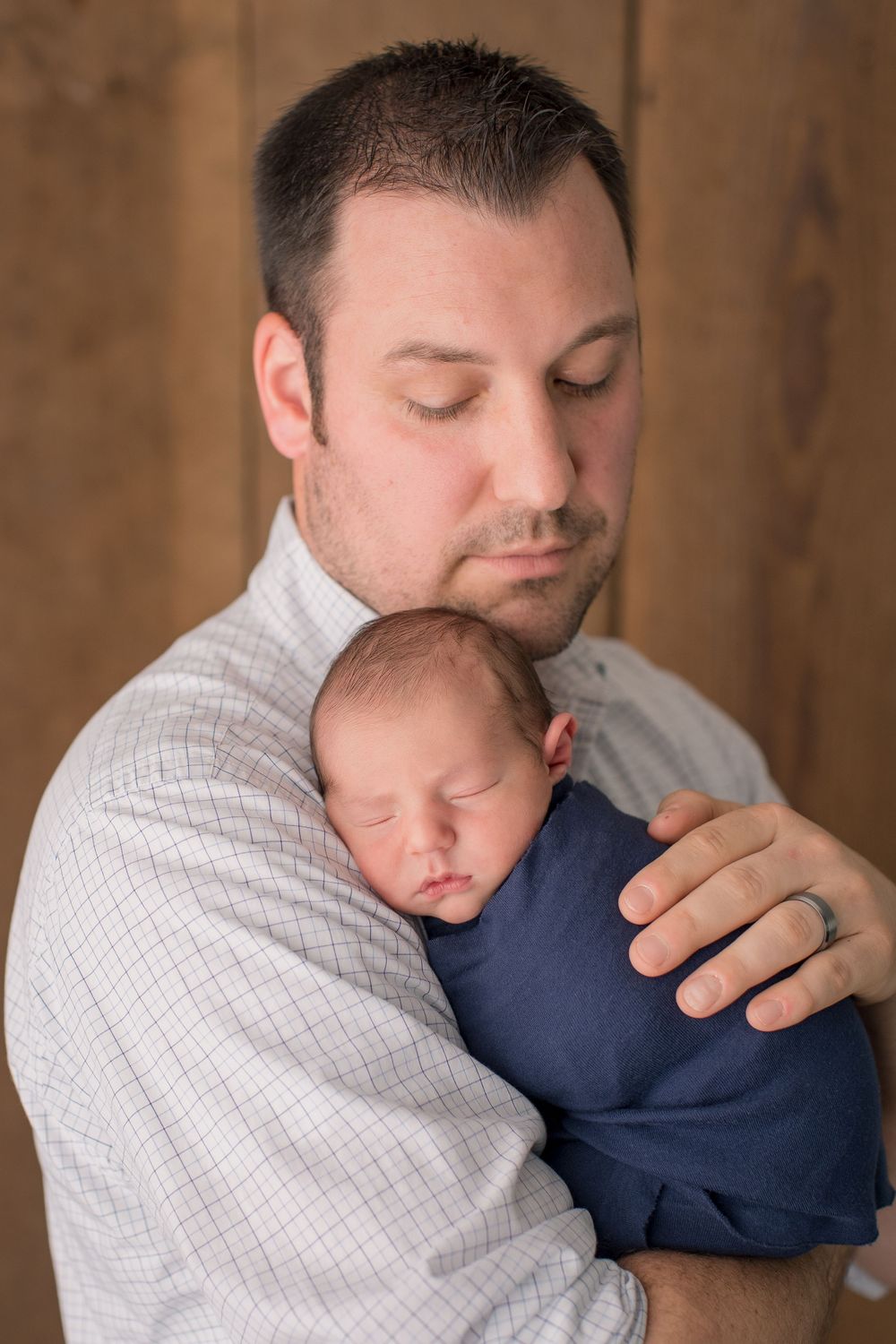 An intimate portrait showing tender moment with sleeping newborn against wood paneled background.