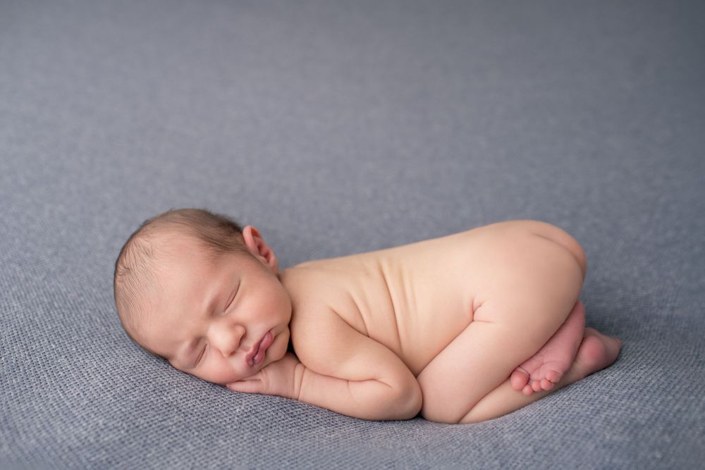 Peaceful sleeping newborn curled up on gray textured backdrop.