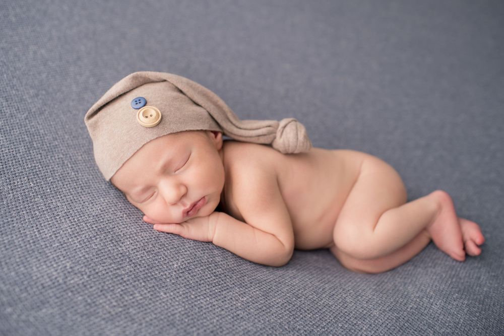 Sleeping newborn wearing tan knit cap on gray background in studio setting.