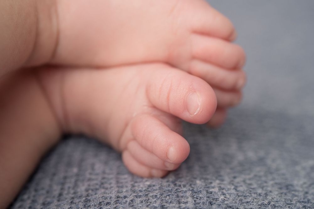 Close-up view of tiny newborn baby toes and feet on soft gray textured fabric background.