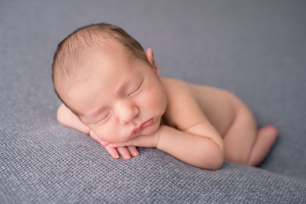 Peaceful sleeping newborn baby curled up on gray textured blanket.