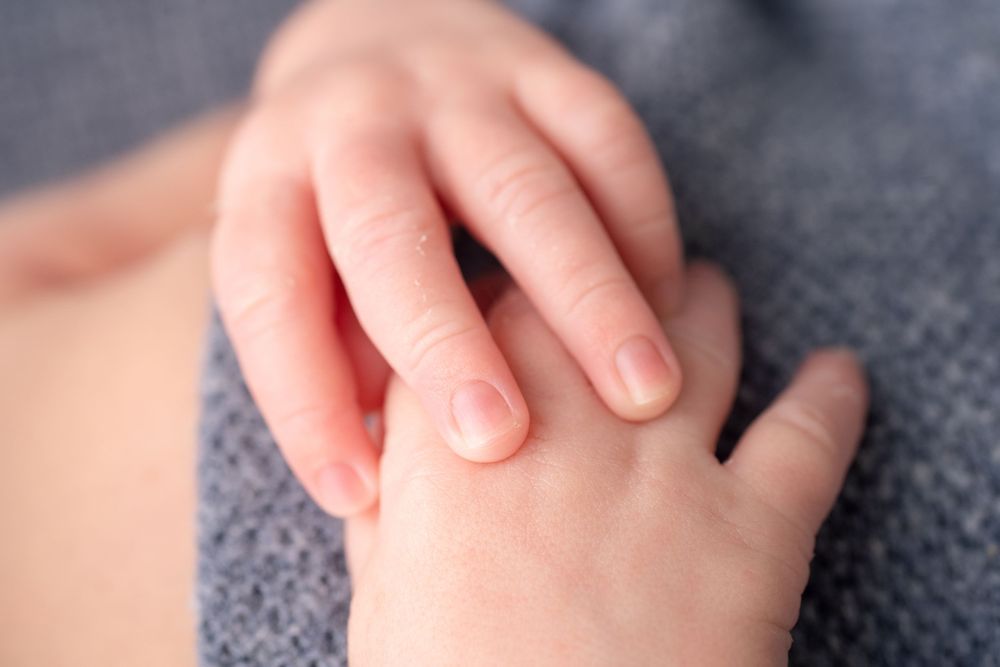 Close-up detail of small baby hands grasping gently against gray textile.