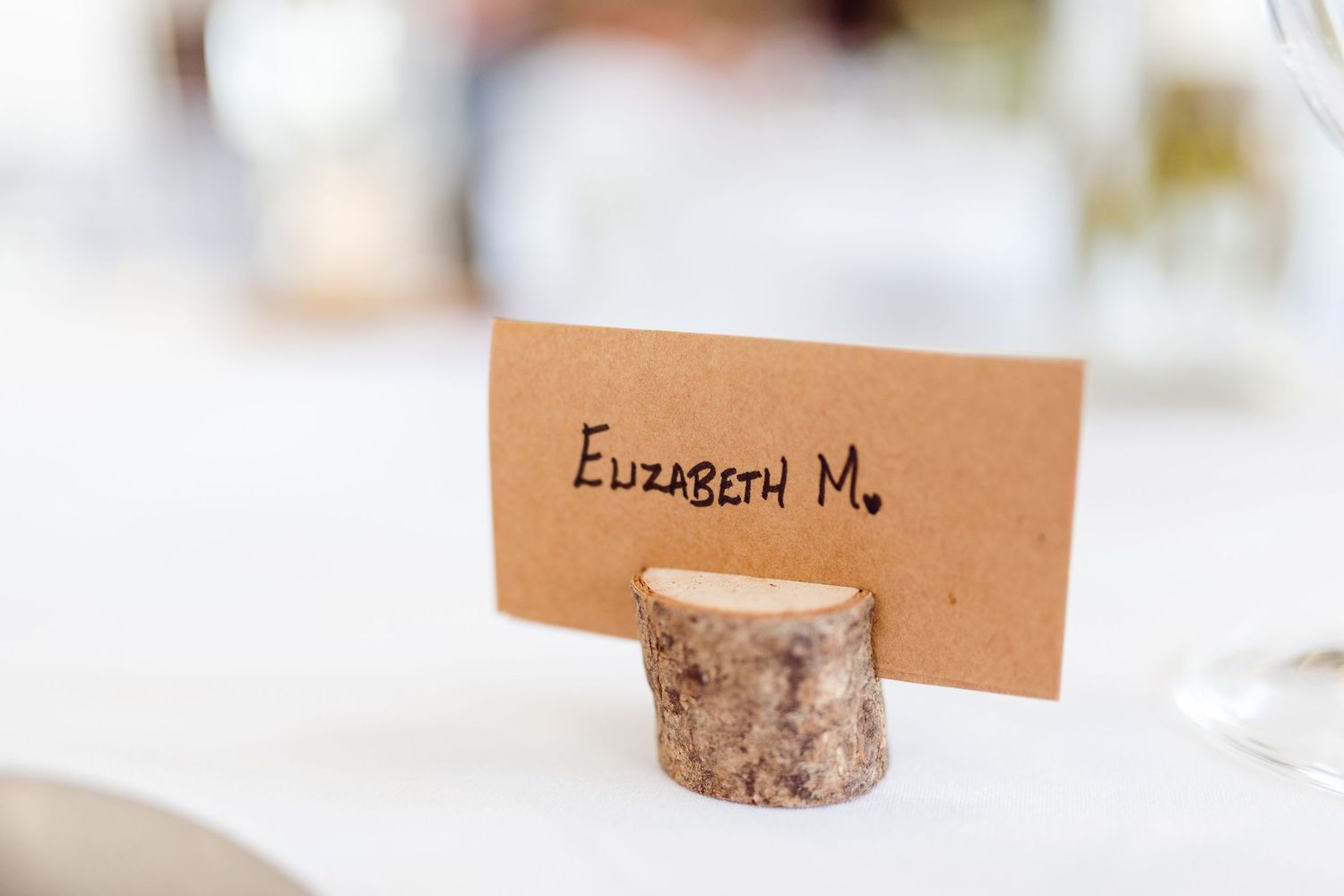 Rustic wood slice place card holder displays name card reading Elizabeth M.