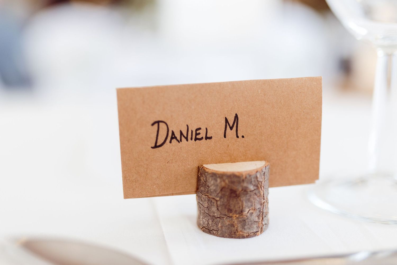Simple kraft paper name card in wooden log holder reads Daniel M.