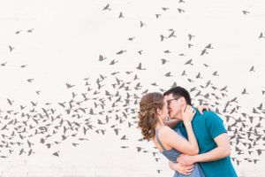 Romantic couple kissing with dramatic flock of birds flying overhead in black and white.