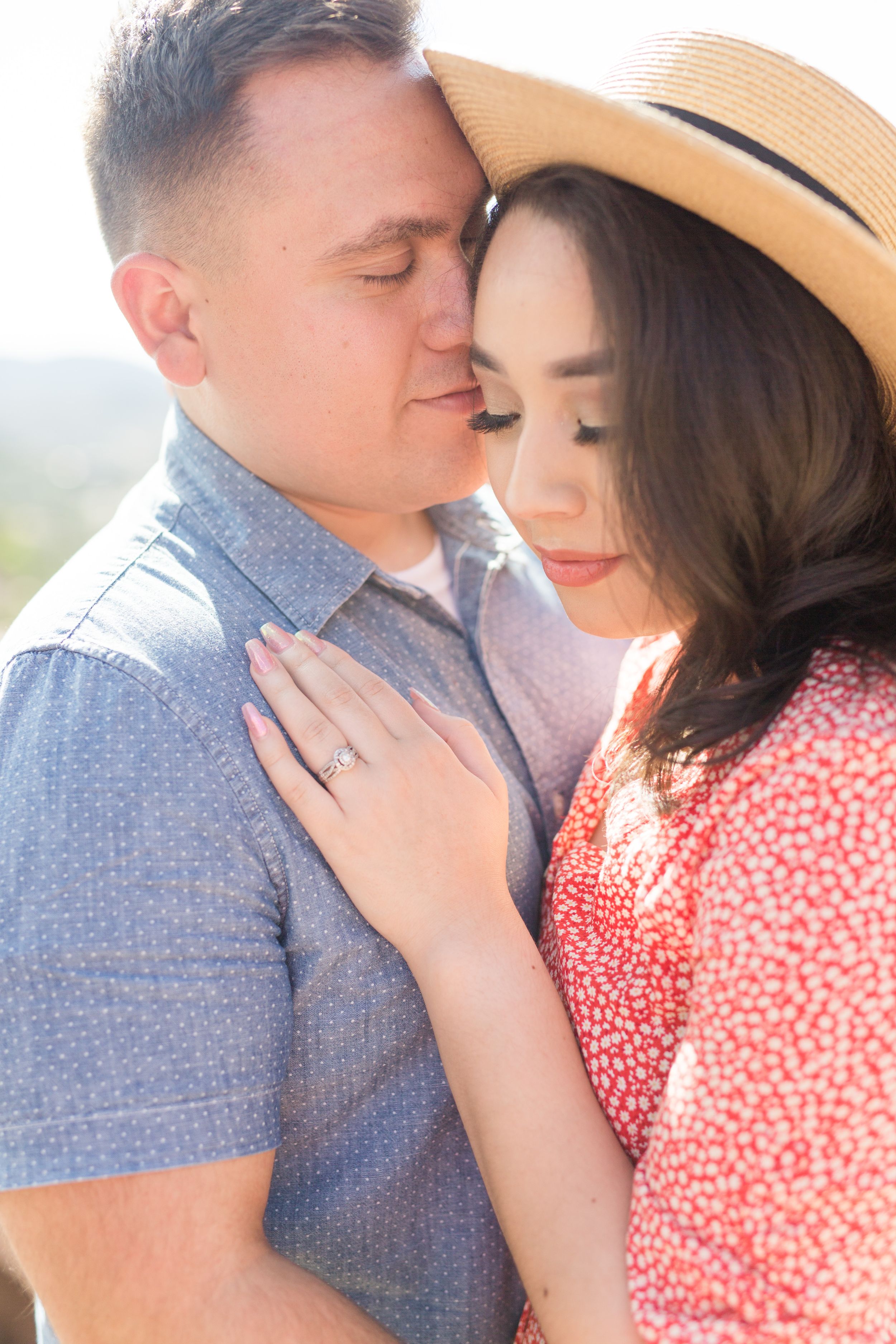 A close intimate moment between a couple in soft sunlight, with one wearing a straw hat.