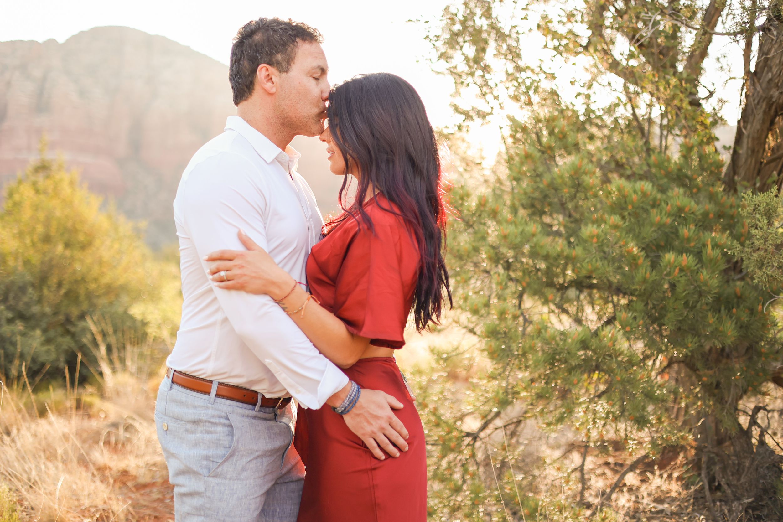 Couple embracing in front of stunning red rock mountains during sunset.