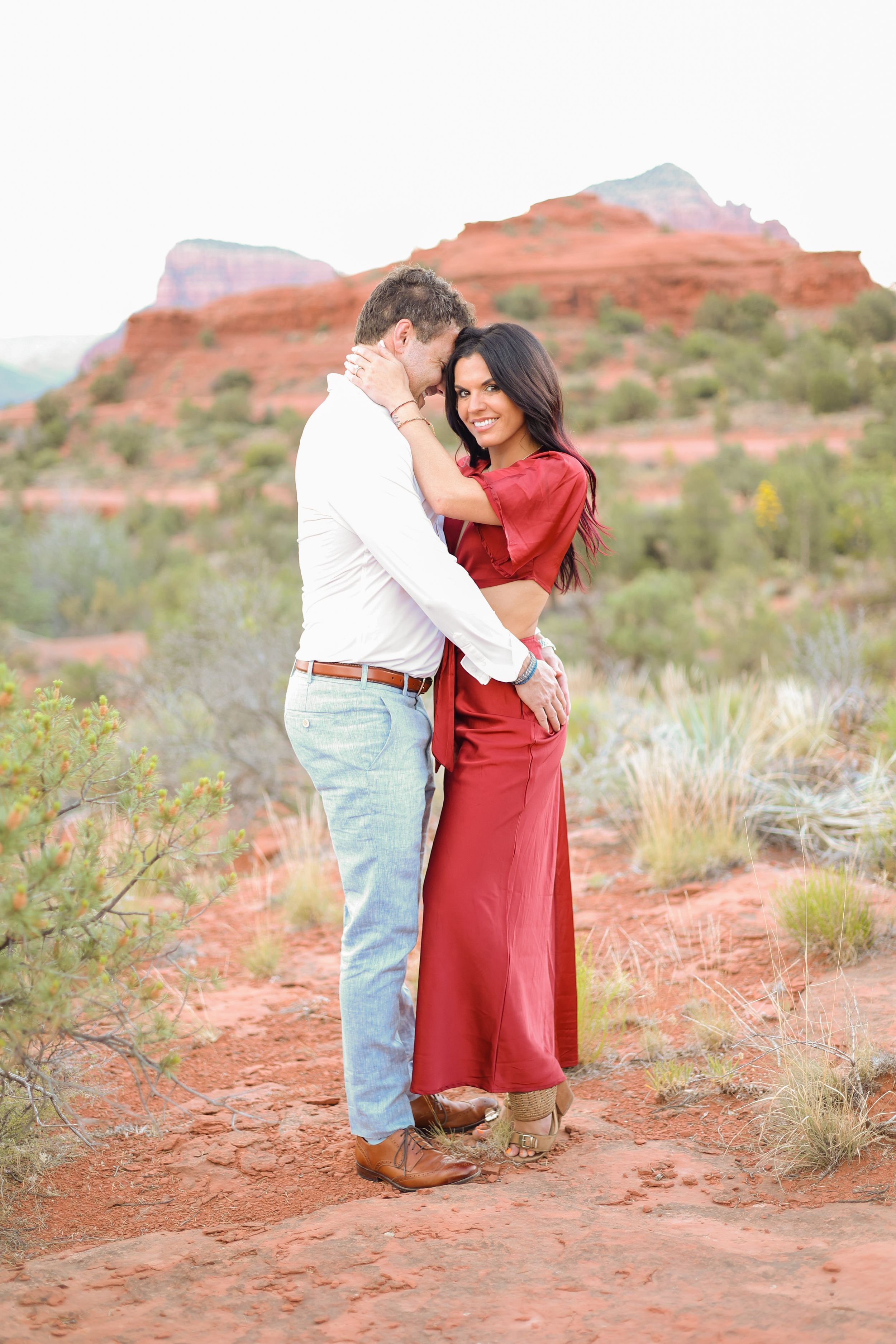 Romantic desert engagement photo with couple embracing on red rock terrain.