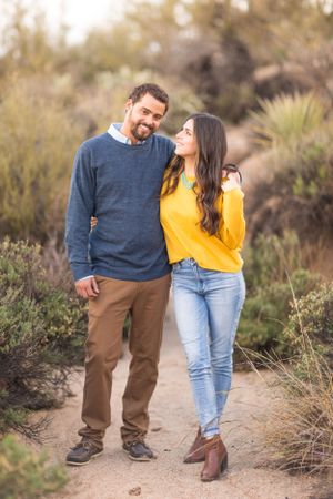 Couple standing together on desert trail surrounded by desert brush at golden hour.